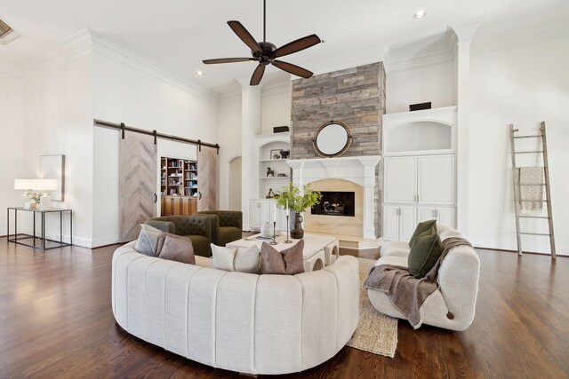 living room featuring a barn door, ceiling fan, a large fireplace, and dark wood-type flooring