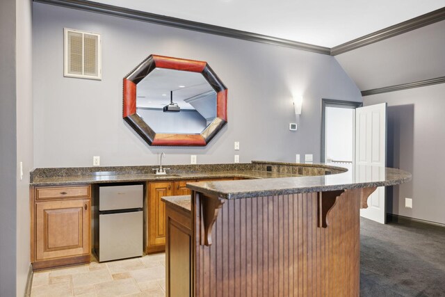 kitchen featuring stainless steel refrigerator, crown molding, a kitchen bar, kitchen peninsula, and light colored carpet