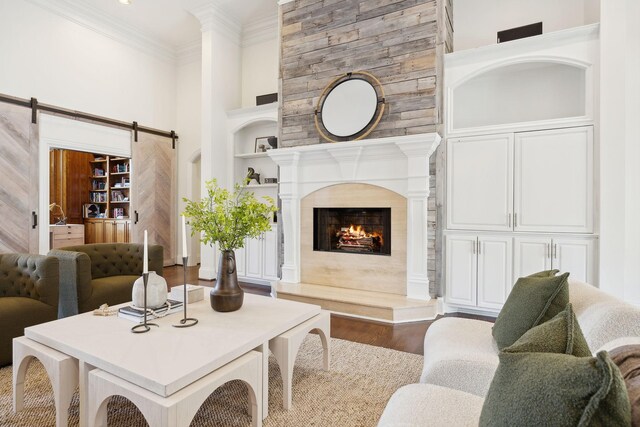 living room with a high end fireplace, a barn door, wood-type flooring, built in features, and ornamental molding