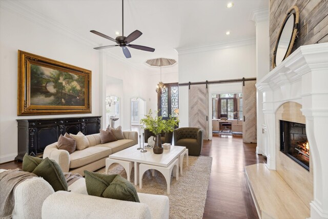 living room with crown molding, a premium fireplace, ceiling fan, dark hardwood / wood-style floors, and a barn door