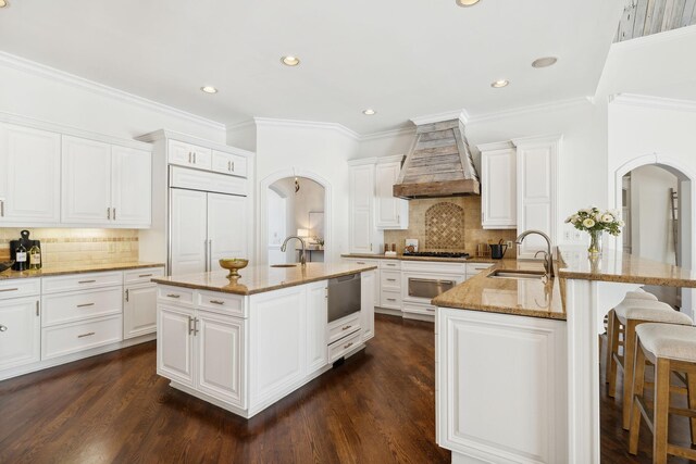 kitchen featuring custom range hood, light stone countertops, sink, dark wood-type flooring, and a kitchen bar