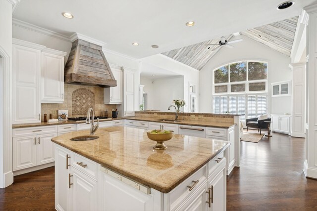 kitchen with a center island with sink, custom range hood, sink, and vaulted ceiling