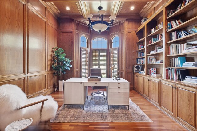 office space featuring light wood-type flooring, built in shelves, coffered ceiling, wood walls, and ornamental molding