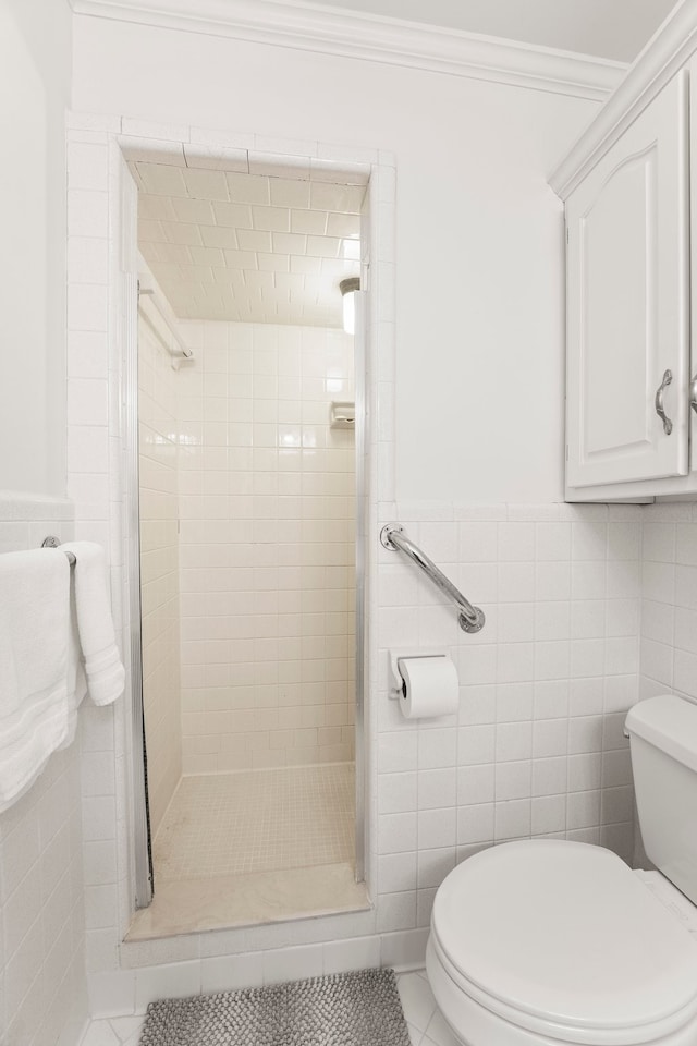 bathroom with tile patterned flooring, toilet, a tile shower, tile walls, and ornamental molding