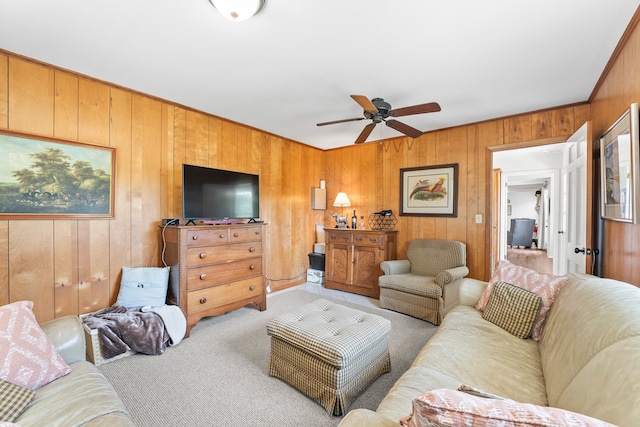 carpeted living room with ceiling fan, wooden walls, and ornamental molding