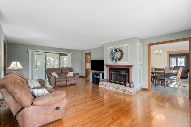 living room featuring an inviting chandelier, light hardwood / wood-style floors, and a brick fireplace