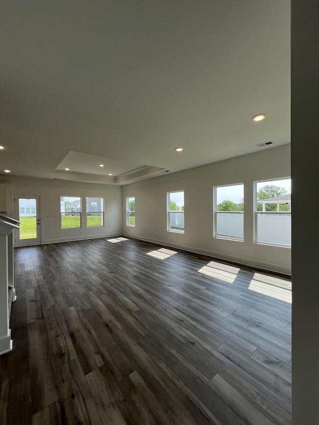 unfurnished living room with recessed lighting, dark wood-type flooring, a tray ceiling, and baseboards