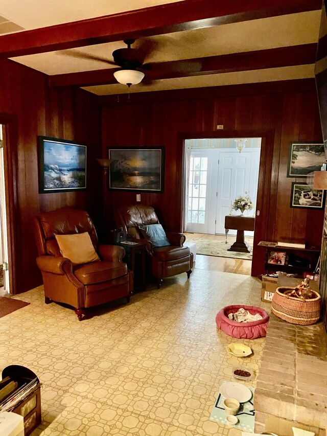 living room with ceiling fan, beamed ceiling, and wooden walls