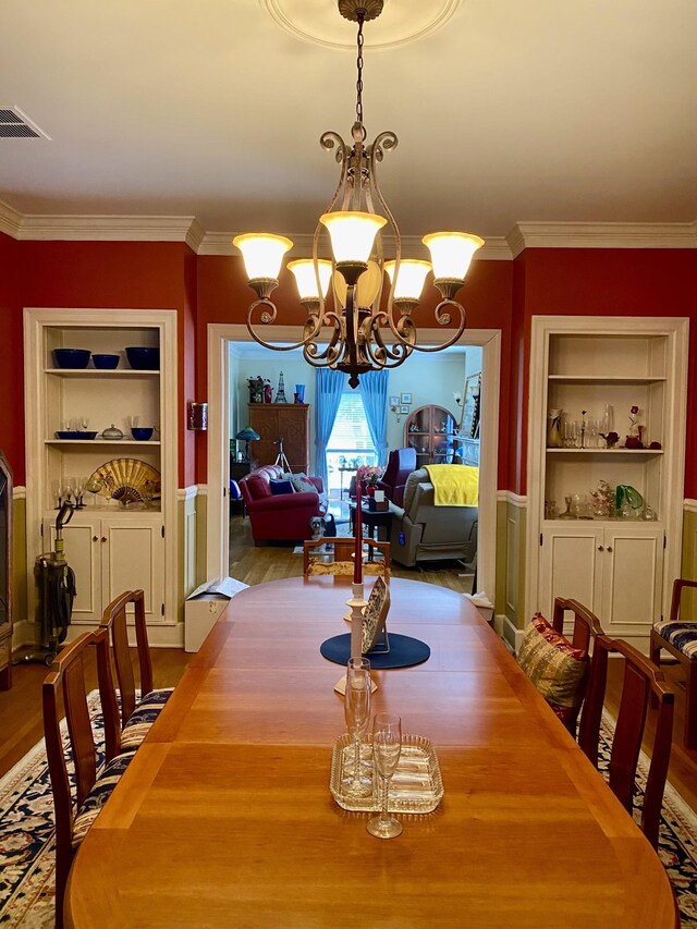 dining space with a notable chandelier, light hardwood / wood-style flooring, built in features, and crown molding