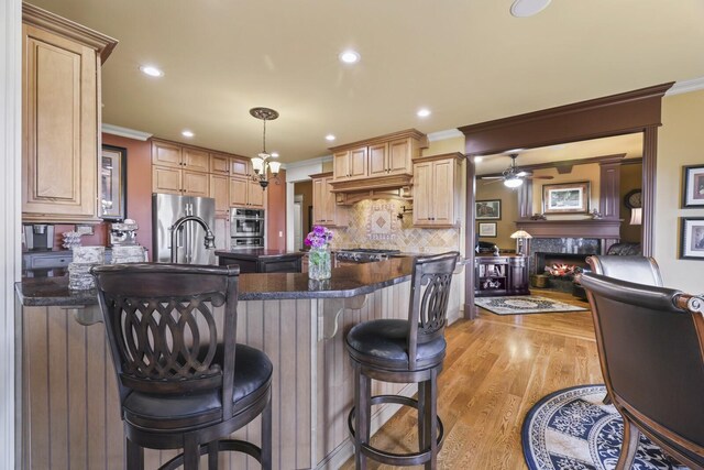 kitchen with a high end fireplace, ceiling fan with notable chandelier, light hardwood / wood-style floors, a breakfast bar, and dark stone counters