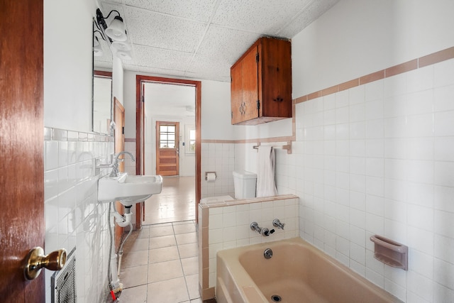 bathroom with tile walls, toilet, tile patterned floors, a paneled ceiling, and a washtub