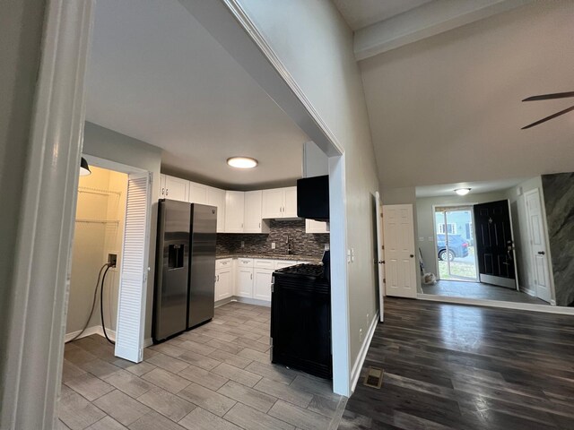 kitchen with black gas range, stainless steel fridge, tasteful backsplash, open floor plan, and white cabinetry