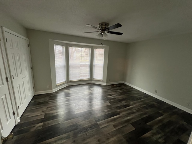 unfurnished bedroom with a closet, baseboards, dark wood finished floors, and a ceiling fan