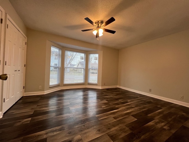 unfurnished room with dark wood-style floors, a textured ceiling, and baseboards