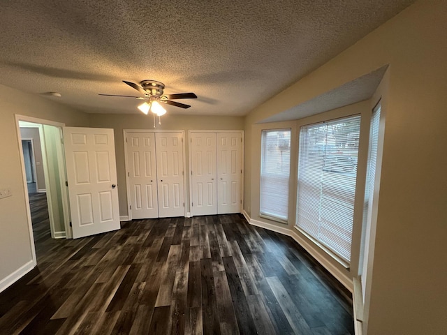 unfurnished bedroom featuring a textured ceiling, baseboards, dark wood finished floors, and two closets