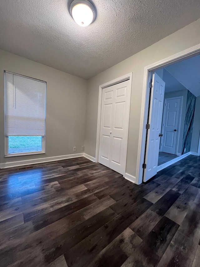 unfurnished bedroom with a textured ceiling, dark wood-type flooring, a closet, and baseboards