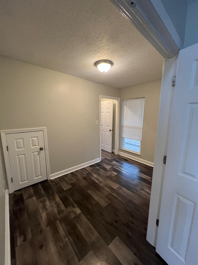 interior space featuring a textured ceiling, dark wood-type flooring, and baseboards