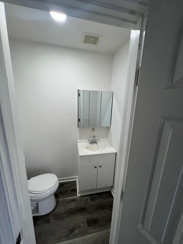 bathroom with baseboards, visible vents, toilet, wood finished floors, and vanity