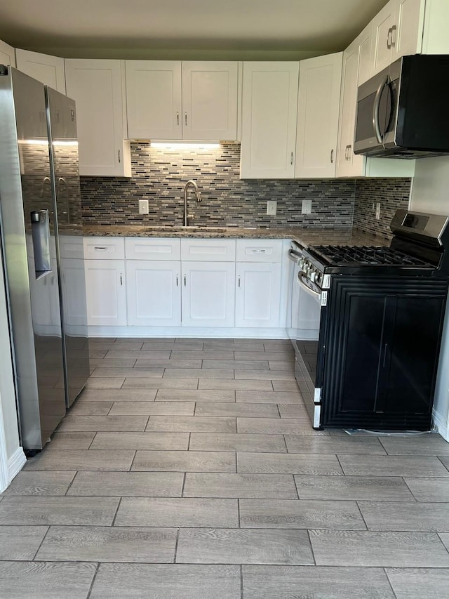 kitchen with stainless steel appliances, dark stone counters, white cabinets, and backsplash