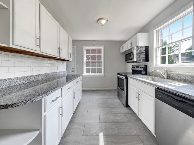 kitchen featuring light stone countertops, appliances with stainless steel finishes, white cabinets, and decorative backsplash