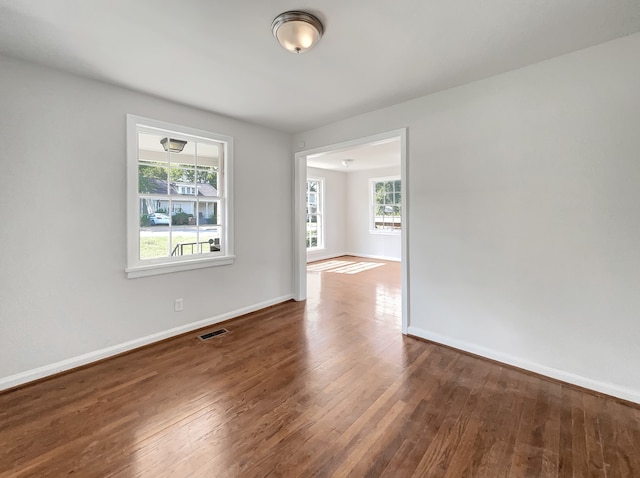 empty room with a wealth of natural light and dark hardwood / wood-style floors