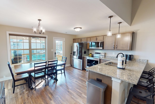 kitchen featuring appliances with stainless steel finishes, light stone countertops, pendant lighting, hardwood / wood-style floors, and a chandelier