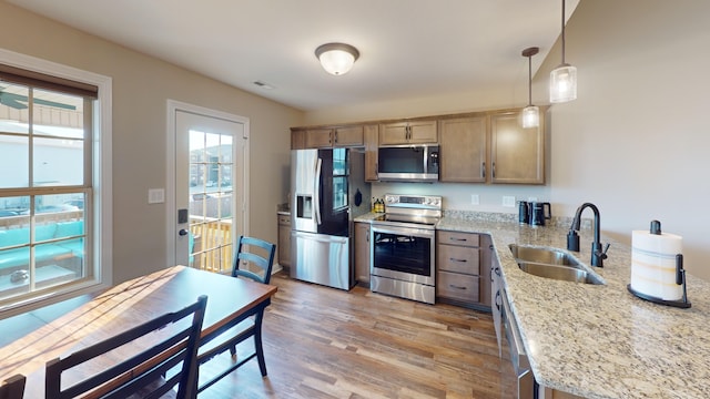 kitchen featuring appliances with stainless steel finishes, light stone countertops, light hardwood / wood-style flooring, decorative light fixtures, and sink