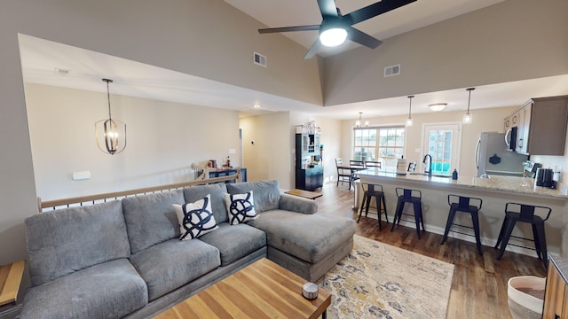 living room with ceiling fan with notable chandelier, sink, dark wood-type flooring, and high vaulted ceiling