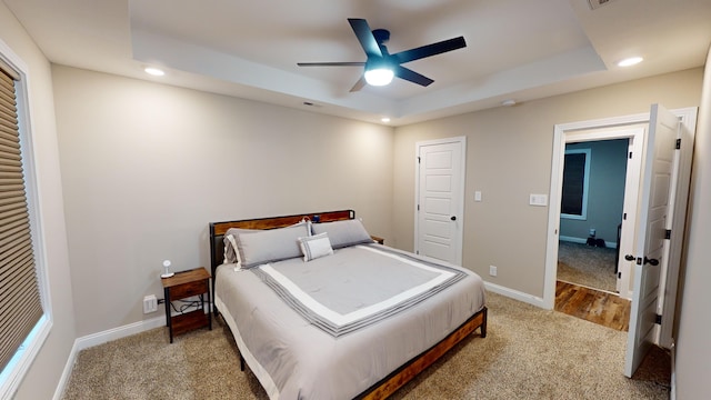 bedroom featuring light carpet, a tray ceiling, and ceiling fan