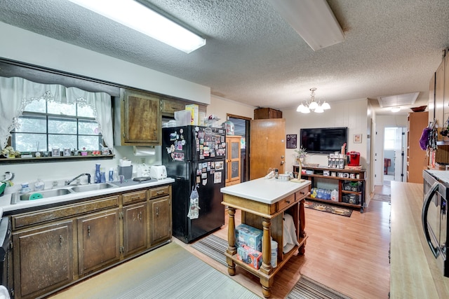 kitchen with black fridge, a notable chandelier, a textured ceiling, sink, and light hardwood / wood-style floors