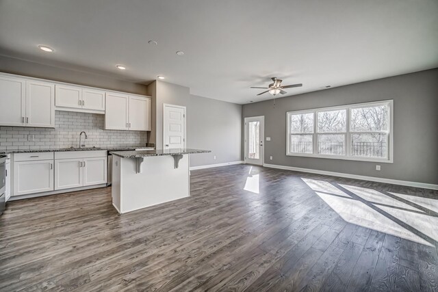 kitchen featuring hardwood / wood-style flooring, a kitchen breakfast bar, a kitchen island, white cabinetry, and dark stone countertops