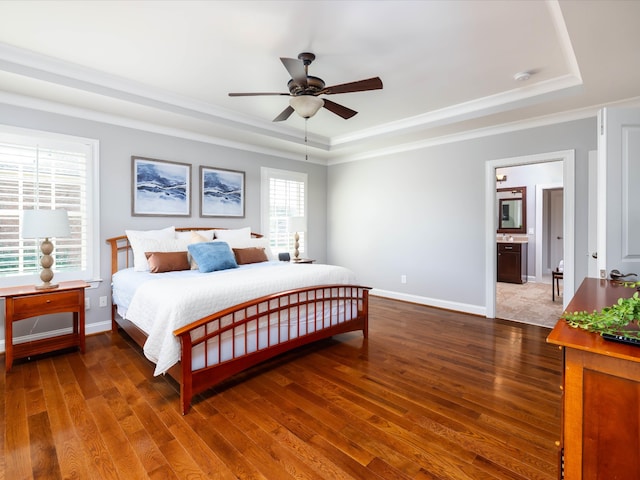 bedroom featuring dark hardwood / wood-style flooring, a tray ceiling, ensuite bath, and ceiling fan