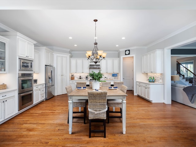 kitchen featuring decorative backsplash, appliances with stainless steel finishes, light hardwood / wood-style flooring, white cabinetry, and hanging light fixtures