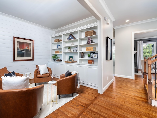 living area featuring wooden walls, ornamental molding, and light wood-type flooring