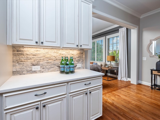 kitchen featuring backsplash, light hardwood / wood-style floors, white cabinetry, and ornamental molding