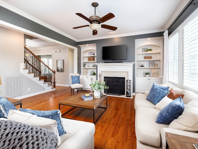 living room with ceiling fan, dark hardwood / wood-style flooring, crown molding, and built in shelves