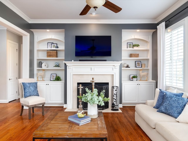 living room featuring ceiling fan, built in features, ornamental molding, and dark wood-type flooring