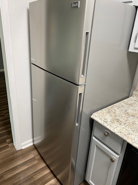 kitchen with stainless steel fridge, light stone countertops, and dark hardwood / wood-style flooring