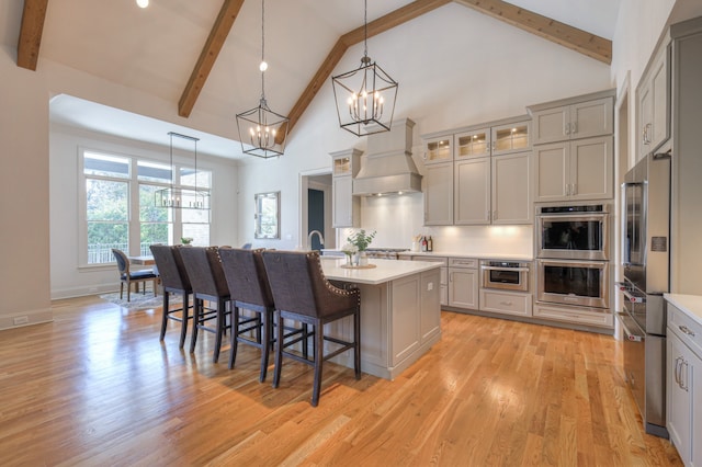 kitchen with a kitchen island with sink, a chandelier, stainless steel appliances, premium range hood, and light hardwood / wood-style floors