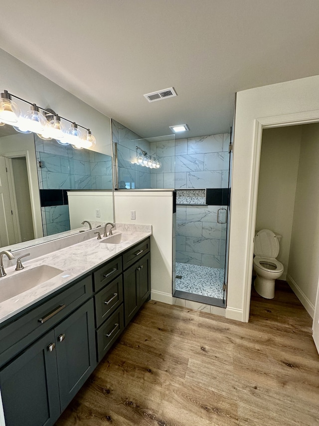 bathroom with hardwood / wood-style floors, a shower with door, toilet, and vanity