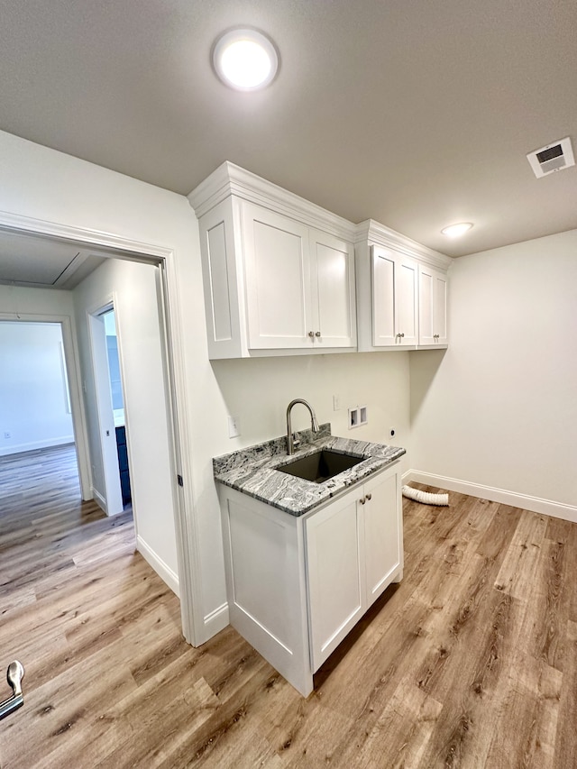 kitchen featuring white cabinets, light stone counters, light hardwood / wood-style floors, and sink