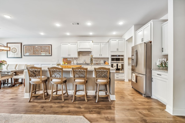 kitchen with a center island with sink, white cabinetry, stainless steel appliances, a kitchen breakfast bar, and light wood-type flooring