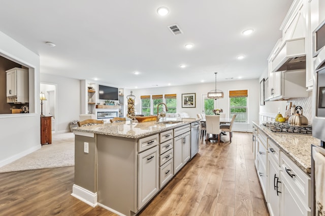 kitchen with hanging light fixtures, light hardwood / wood-style floors, stainless steel appliances, a kitchen island with sink, and sink