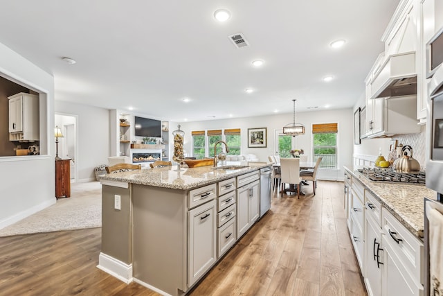 kitchen featuring appliances with stainless steel finishes, light hardwood / wood-style floors, decorative light fixtures, a kitchen island with sink, and sink