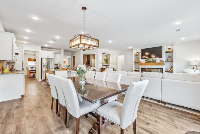 dining area featuring a notable chandelier, light wood-type flooring, and a multi sided fireplace