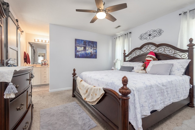 carpeted bedroom with a barn door, ceiling fan, and ensuite bathroom