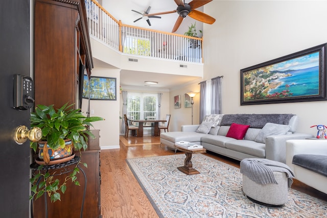 living room featuring ceiling fan, a towering ceiling, and light hardwood / wood-style floors