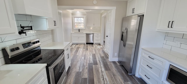 kitchen featuring appliances with stainless steel finishes, white cabinetry, sink, wood-type flooring, and decorative backsplash