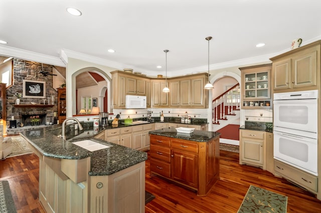 kitchen featuring white appliances, decorative light fixtures, a center island, a stone fireplace, and dark wood-type flooring