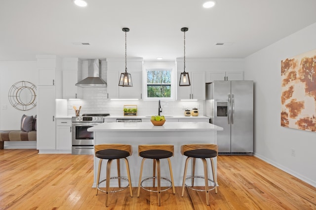 kitchen featuring white cabinets, wall chimney exhaust hood, light wood-type flooring, and appliances with stainless steel finishes